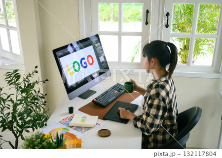 Graphic designer creating logo on digital tablet in bright modern workspace with computer and color palette 132117804