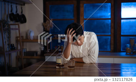 Depressed man sitting alone with glass of alcohol at night, symbol of loneliness and stress 132117826