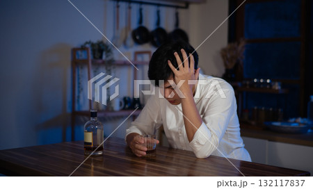 Depressed man sitting alone with glass of alcohol at night, symbol of loneliness and stress Depressed man sitting alone with glass of alcohol at night, symbol of loneliness and stress 132117837