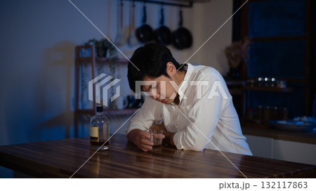 Depressed man sitting alone with glass of alcohol at night, symbol of loneliness and stress Depressed man sitting alone with glass of alcohol at night, symbol of loneliness and stress 132117863