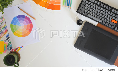 Top view of creative workspace with color palette, digital tablet, and notebook sketching logo design on clean white desk 132117896