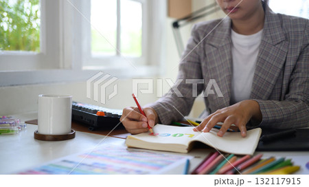 Closeup creative woman sketching logo ideas in notebook with color samples and pencils in bright modern workspace Closeup creative woman sketching logo ideas in notebook with color samples and pencils in bright modern workspace 132117915