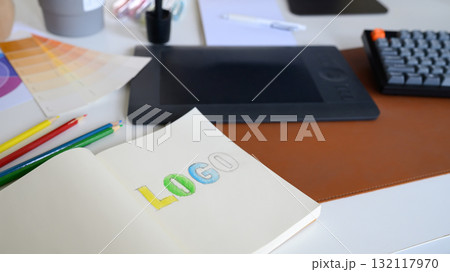 Close-up of logo sketch with color pencils, palette, and tablet on designer workspace in modern creative office 132117970