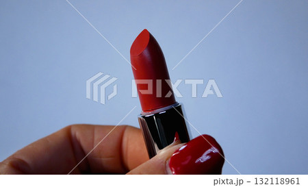 Woman's hand with red manicure holds and twists open a red lipstick. Woman's hand with red manicure holds and twists open a red lipstick. 132118961