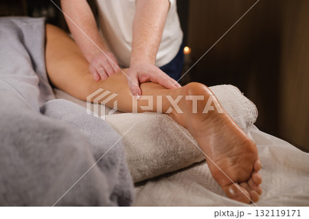 Relaxation session featuring a massage on a woman's leg in a cozy spa environment with soft lighting and calming decor 132119171
