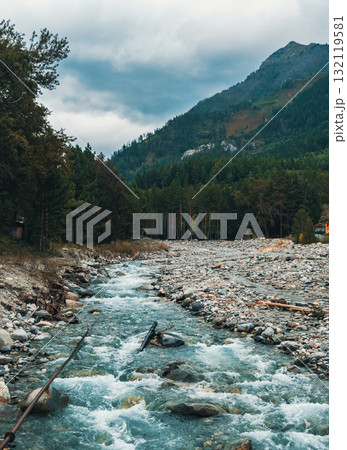 Serene river flowing through rocky landscape in mountains under overcast sky near forest 132119581