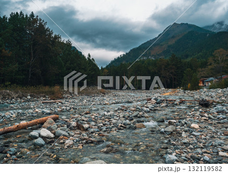 Serene river flowing through rocky landscape in mountains under overcast sky near forest 132119582