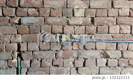 Close up of a brick wall with a light switch and blue and green pipes running along the wall surface 132122111