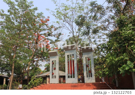 A striking monument with tall, white pillars stands amidst lush green trees and foliage, under a bright sky 132122703