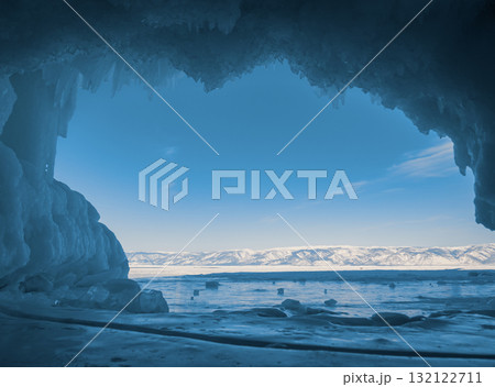 Stunning view of Baikal Lake through an icy cave during winter with crystal clear blue sky and distant snow-covered mountains 132122711