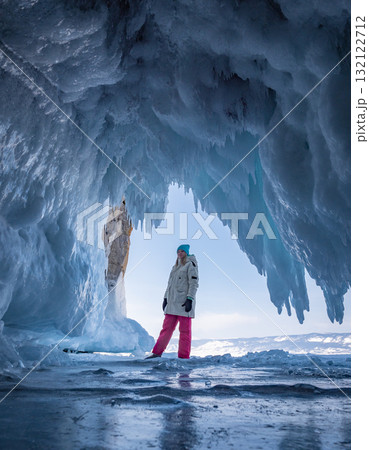 Young woman in winter gear stands inside a stunning ice cave on Baikal Lake. Young woman in winter gear stands inside a stunning ice cave on Baikal Lake. 132122712