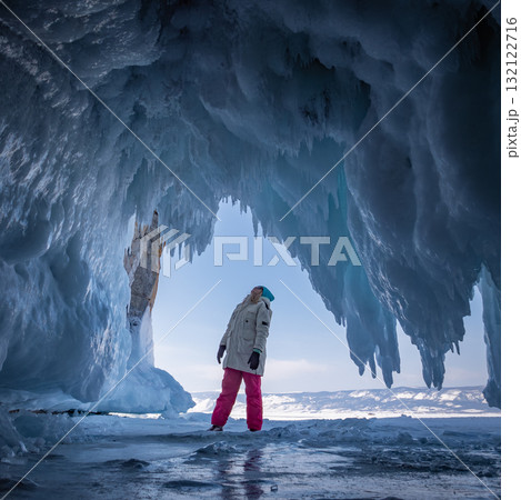 Young woman in winter gear stands inside a stunning ice cave on Baikal Lake. 132122716