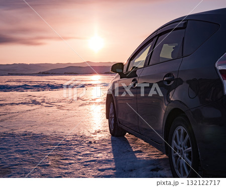 Winter sunset over Baikal Lake with a car parked near the frozen shoreline showcasing natural beauty and serene landscapes 132122717