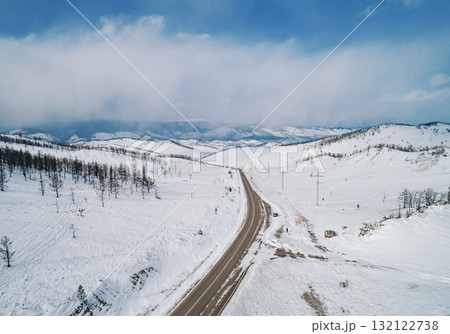 Snow-covered winding road through a winter landscape with blue sky in the background Snow-covered winding road through a winter landscape with blue sky in the background 132122738