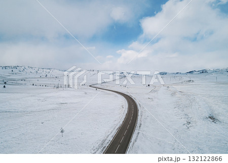 Snow-covered winding road through a winter landscape with blue sky in the background Snow-covered winding road through a winter landscape with blue sky in the background 132122866