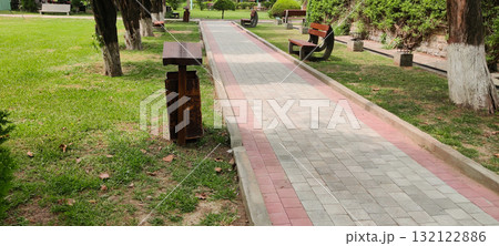 Empty Benches in Park Along Walking Track Surrounded by Trees Grass and Garbage Can Symbolize Solitude and Calmness Empty Benches in Park Along Walking Track Surrounded by Trees Grass and Garbage Can Symbolize Solitude and Calmness 132122886