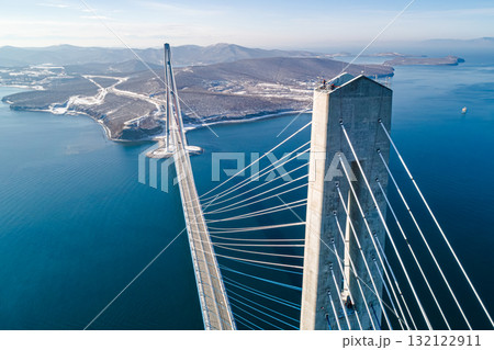 Aerial view of the cable-stayed bridge in Vladivostok, highlighting its towering pillars and cables against a backdrop of clear skies and calm waters 132122911