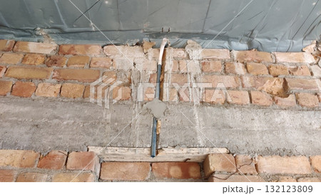 Exposed brick wall with cement repairs and a blue pipe running vertically through the center area 132123809