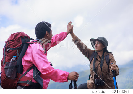 Two hikers giving high five on mountain peak with backpacks, symbol of success, teamwork, motivation, friendship, encouragement, outdoor adventure and achievement in travel lifestyle. 132123861
