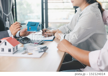Close up of real estate agent showing small house model to client with calculator, contract paperwork on desk, concept of mortgage loan, home ownership, property investment agreement. mortgage loan 132124014
