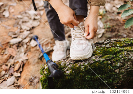 Close up of hiker tying shoelaces on sneaker with trekking pole in forest, symbol of preparation, adventure, outdoor lifestyle, hiking, journey and exploration in nature trail. adventure hiking 132124092