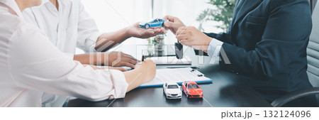 Panorama view of car dealer handing key and vehicle model to customer during contract signing, concept of auto loan, finance, leasing, insurance, purchase agreement and business success. auto loan. 132124096