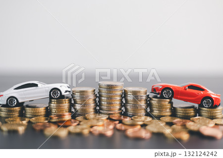 Red and white car models with open doors positioned beside stacked coins, symbolizing car loan, auto finance, insurance, investment, wealth, savings and money management concept. 132124242
