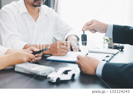Customer receiving car key from dealer after signing contract, successful auto purchase and finance agreement at office desk, concept of vehicle loan, leasing, insurance or ownership. vehicle loan. 132124243