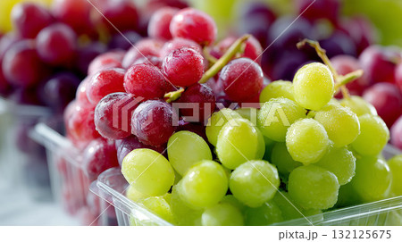Fresh red and green grapes with water droplets in plastic containers under bright light Fresh red and green grapes with water droplets in plastic containers under bright light 132125675