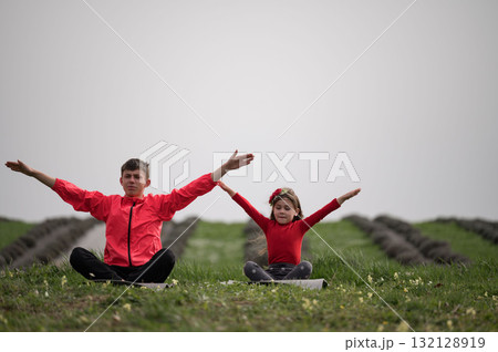 Two joyful children practicing yoga in a serene green field surrounded by rows of earth and budding flowers in the embrace of a cloudy morning sky 132128919