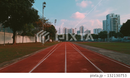 Red athletic track leading towards city skyline under a clear blue sky with scattered clouds 132130753