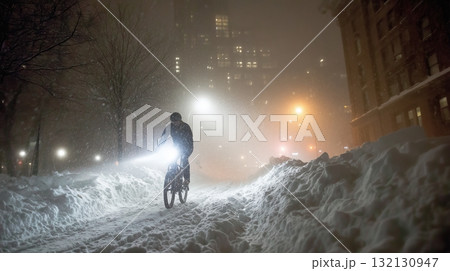 Bicyclist navigating snowy urban street at night with bright headlights illuminating path Bicyclist navigating snowy urban street at night with bright headlights illuminating path 132130947