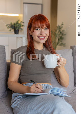 Young woman slowly drinks hot tea writes tomorrow task list in notebook relax and calm after stress Young woman slowly drinks hot tea writes tomorrow task list in notebook relax and calm after stress 132131557