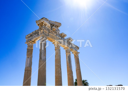 Ancient Columnar Structure Beneath a Vibrant Blue Sky with Sunlight Illuminating the Historic Architecture and Captivating Nature Surrounding It 132131570