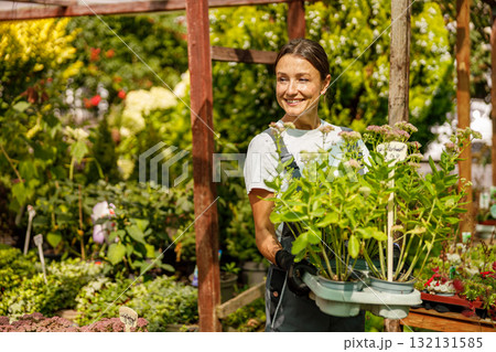 A Smiling Gardener is Surrounded by Fresh Plants in a Beautiful and Lush Nursery Setting A Smiling Gardener is Surrounded by Fresh Plants in a Beautiful and Lush Nursery Setting 132131585