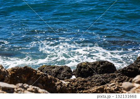 Captivating View of Gentle Waves Interacting with Rocky Shoreline Under Bright Sunny Daylight Captivating View of Gentle Waves Interacting with Rocky Shoreline Under Bright Sunny Daylight 132131668