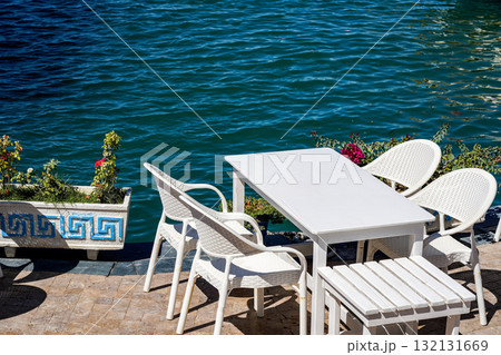 A Tranquil Waterfront Scene Featuring White Furniture and Calm Waters Surrounded by Lush Greenery and Colorful Flowers A Tranquil Waterfront Scene Featuring White Furniture and Calm Waters Surrounded by Lush Greenery and Colorful Flowers 132131669