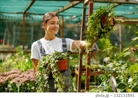 A Happy Woman Enjoying Gardening amidst a Beautiful and Lush Plant Nursery Environment 132131691