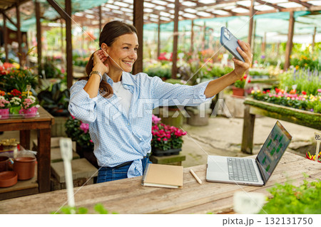 Today, a cheerful woman is capturing a selfie within her vibrant flower shop workspace 132131750