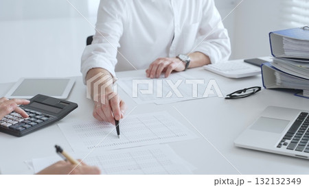 Professional women collaborating, reviewing financial reports using calculator, laptop, discussing workplace strategy with team. Audit and taxes in business 132132349