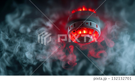 Ceiling smoke detector activated with glowing red light surrounded by dense swirling smoke creating a clear fire alarm and emergency warning scene. 132132701