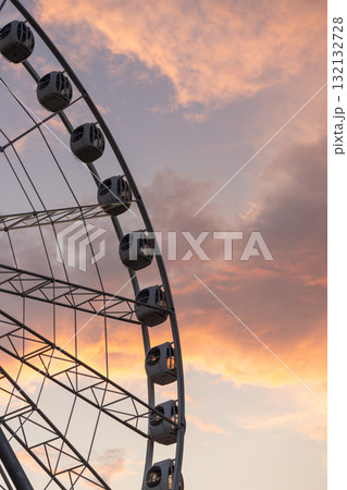 large Ferris wheel against a cloudy sky. The Ferris wheel is surrounded by sunset clouds. 132132728
