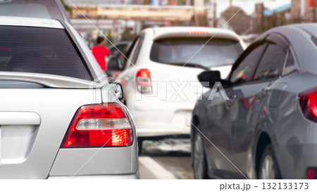 Rear side view of silver car with turn on brake light. Trffic jam on the aspahlt road in the day time. Many cars in the city in business time. 132133173
