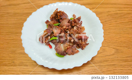 Fried pork with chili peppers served on white plate on wooden table 132133805