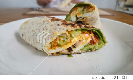 Vegetarian wrap sandwich with fresh vegetables and avocado on white plate 132133812