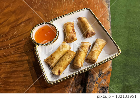 Deep fried Filipino pork lumpia spring roll with dipping sauce on a plate on a natural wooden table Deep fried Filipino pork lumpia spring roll with dipping sauce on a plate on a natural wooden table 132133951