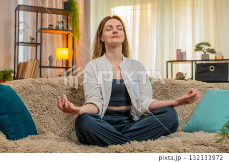 Woman meditating peacefully on home sofa, calm expression, eyes closed, relaxation, taking a break Woman meditating peacefully on home sofa, calm expression, eyes closed, relaxation, taking a break 132133972