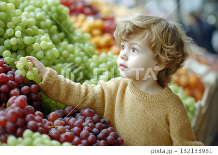 Little child in a warm sweater picking green grapes at a vibrant fruit market surrounded by colorful bunches of fresh grapes Little child in a warm sweater picking green grapes at a vibrant fruit market surrounded by colorful bunches of fresh grapes 132133981