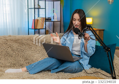 Woman blogger happily recording podcast vlog on sofa actively gesturing telling interesting story Woman blogger happily recording podcast vlog on sofa actively gesturing telling interesting story 132134010