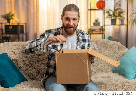 Young man receives delivery at home, sofa unboxing, quick happiness, big reveal, looking at camera Young man receives delivery at home, sofa unboxing, quick happiness, big reveal, looking at camera 132134054